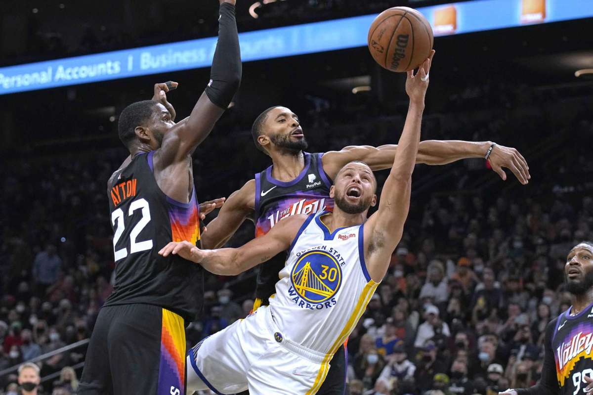 El escolta de los Golden State Warriors Stephen Curry (30) dispara entre el centro de los Phoenix Suns Deandre Ayton (22) y el escolta Cameron Payne durante la primera mitad de un juego de baloncesto de la NBA el sábado 25 de diciembre de 2021 en Phoenix.