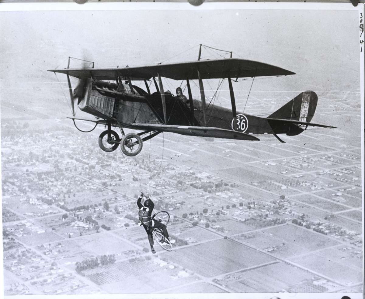 Daredevil Al Johnson "monta una bicicleta" en el aire después de caer del avión y ser suspendido por una cuerda. Esta foto fue tomada sobre el sur de California en 1925.