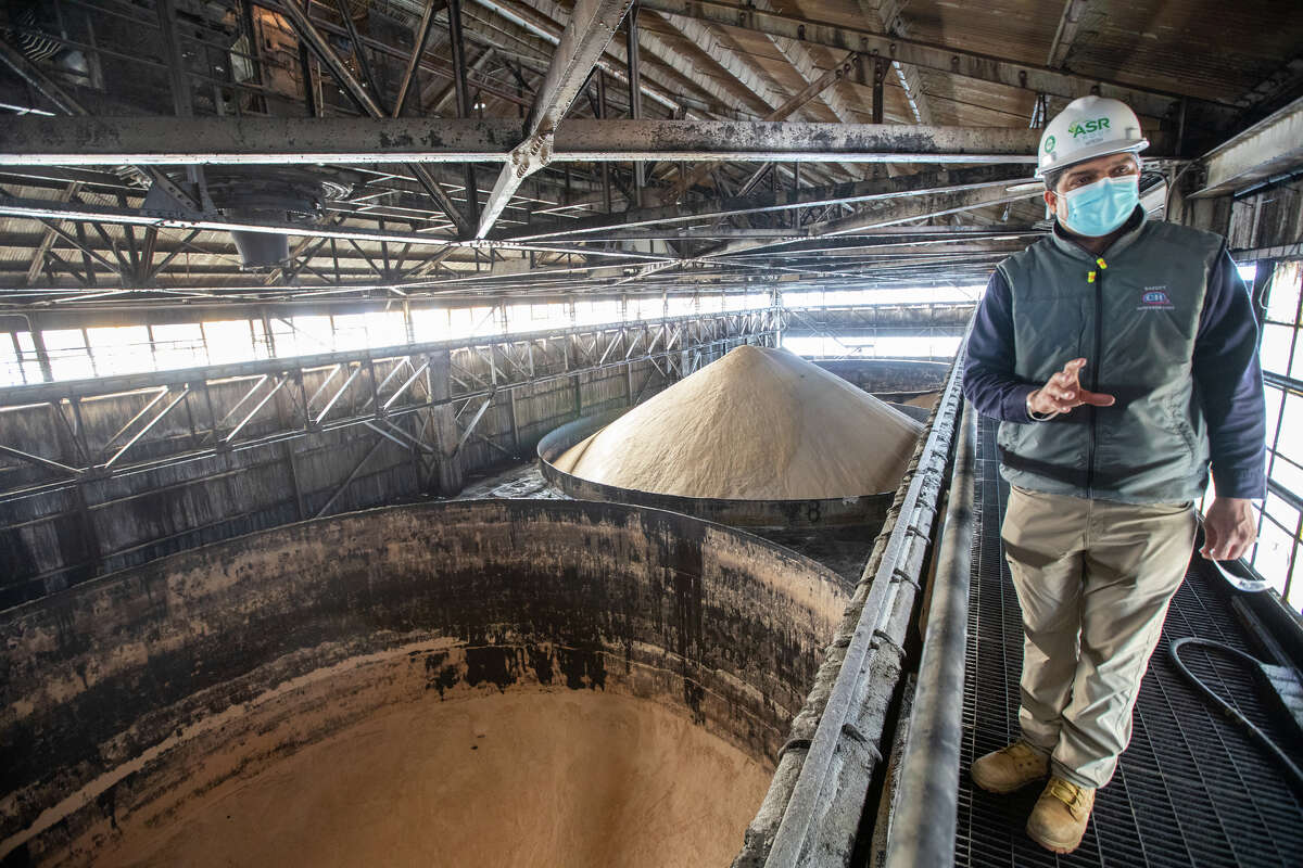 El gerente de planta, Hitesh Modgil, muestra dónde se almacena el azúcar sin refinar en algunos de los nueve enormes silos de azúcar sin refinar en la refinería C&H en Crockett, California, el 2 de marzo de 2022.