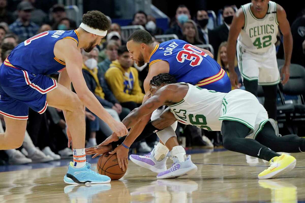 El escolta de los Boston Celtics, Marcus Smart, abajo, alcanza el balón contra el escolta de los Golden State Warriors, Stephen Curry (30) y el escolta Klay Thompson, a la izquierda, durante la primera mitad de un partido de baloncesto de la NBA en San Francisco, el miércoles 16 de marzo de 2022. Curry dejó el juego después de esta jugada.