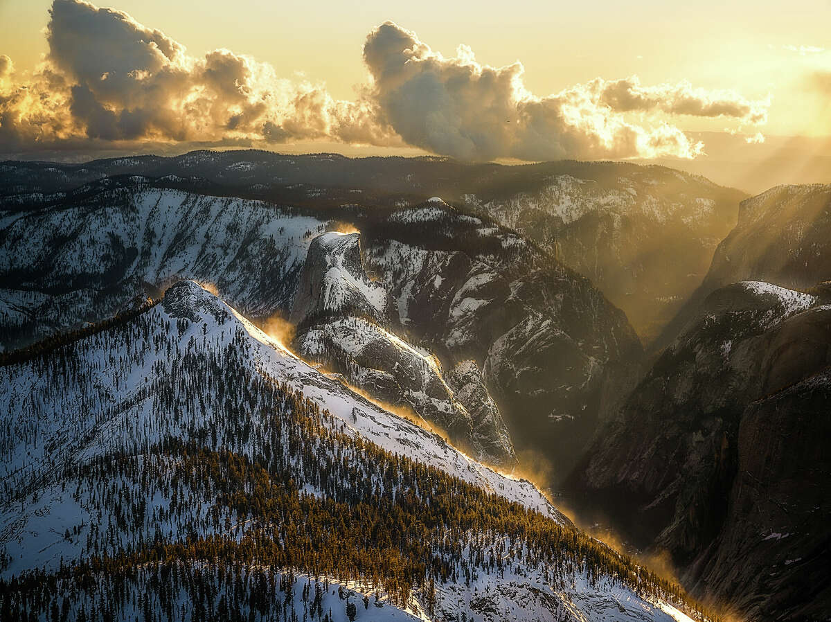 Los rayos del sol brillan de color naranja sobre la nieve que cae de la cima de una montaña en el Parque Nacional Yosemite.