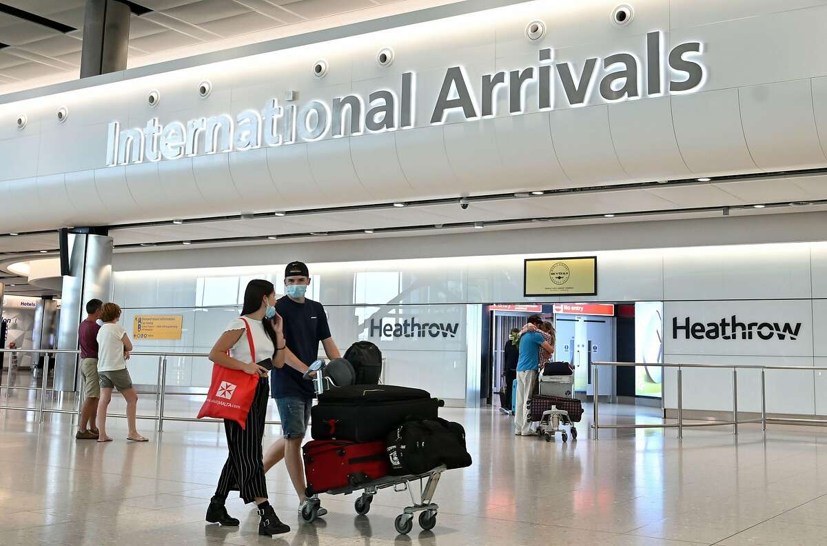 Los pasajeros que usan equipo de protección personal, incluida una máscara facial como medida de precaución contra COVID-19, caminan por la sala de llegadas el 9 de mayo de 2020, después de aterrizar en la Terminal Dos del Aeropuerto Heathrow de Londres en el oeste de Londres.