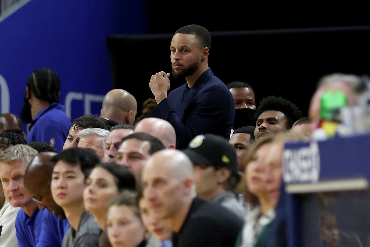 El escolta de los Golden State Warriors, Stephen Curry, arriba, observa desde la banca durante la segunda mitad de un partido de baloncesto de la NBA contra los San Antonio Spurs en San Francisco, el domingo 20 de marzo de 2022.