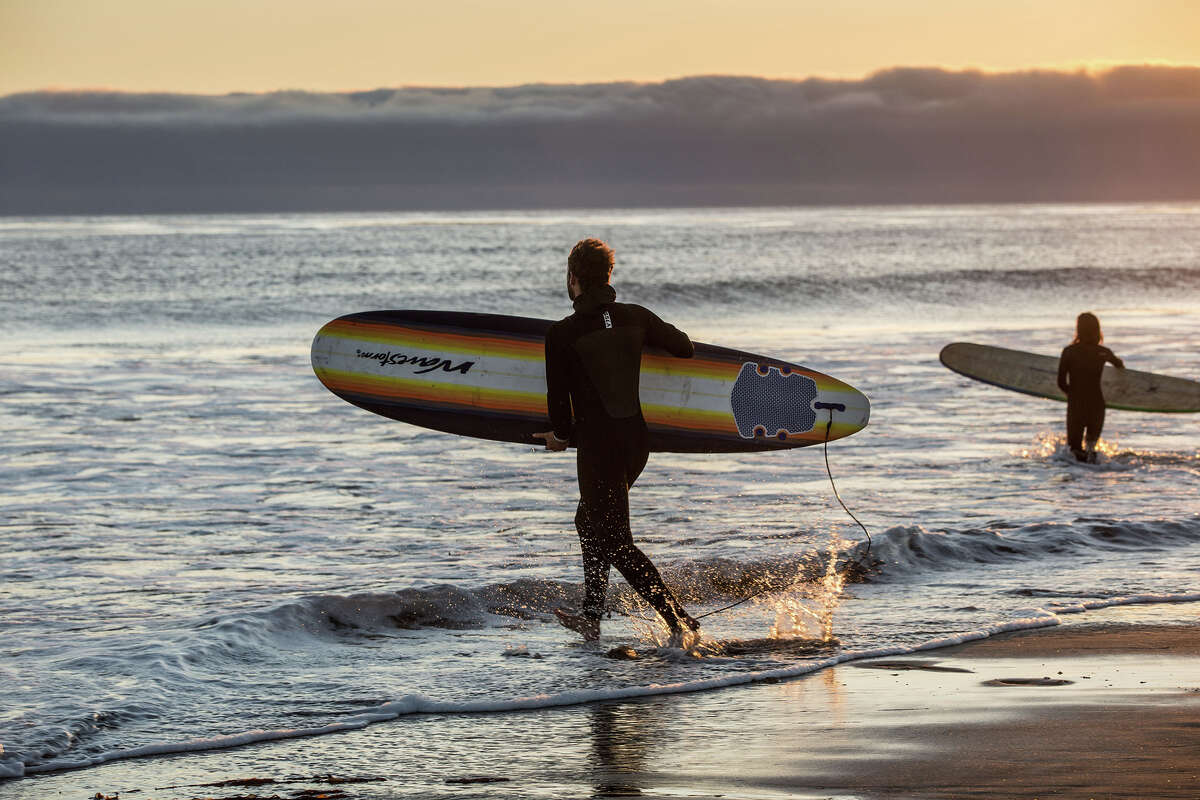 Los surfistas se adentran en el agua al atardecer cuando se forma un espeso banco de niebla frente a la costa en Jalama Beach, California, junto a Hollister Ranch.