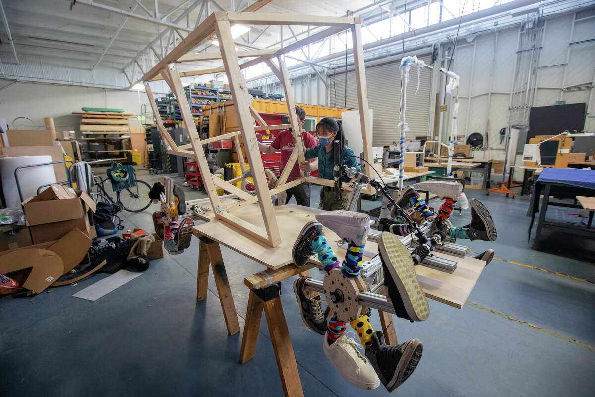 Los empleados de Exploratorium, de izquierda a derecha, Sam Haynor y Gaia Liu montan un corredor de caja de jabón llamado "Muni Toons" están trabajando en el taller del museo en San Francisco el 6 de abril de 2022. El equipo participará en el Soapbox Derby en McLaren Park este domingo.