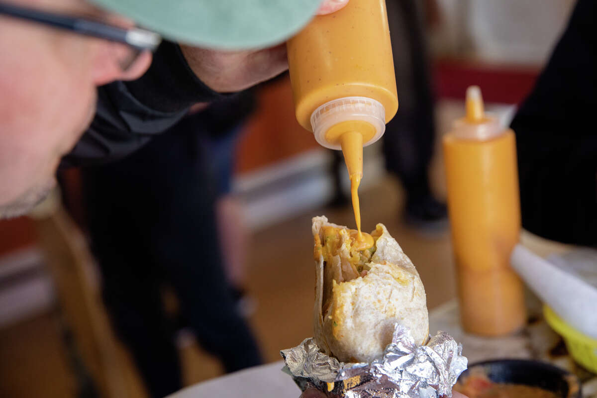El cliente Ryan Damm pone la salsa de naranja exclusiva de La Victoria Taqueria en su burrito en un restaurante en San José, California, el 10 de mayo de 2022.