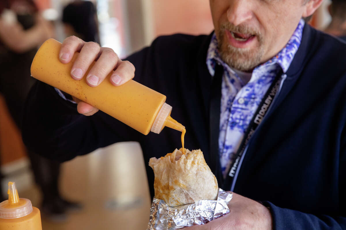 El cliente Shane Mario Ruggieri coloca la salsa de naranja exclusiva de La Victoria Taqueria en su burrito en un restaurante en San José, California, el 10 de mayo de 2022.