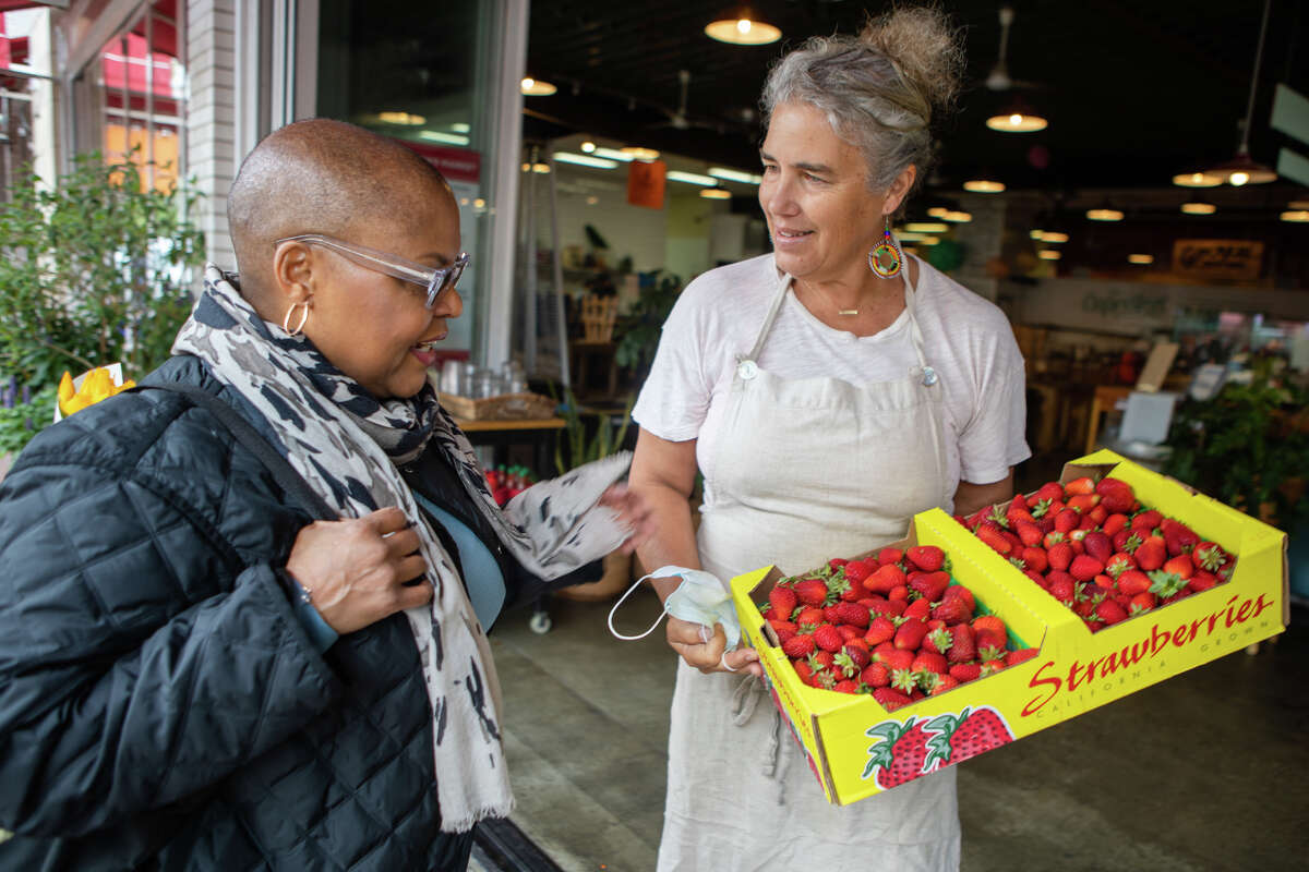 La chef Tonya Holland (izquierda) mira las fresas que su amigo Romney Steele, propietario de The Cook and Her Farmer, acaba de comprar en el mercado de agricultores en Old Town Oakland en Oakland, California, el 6 de mayo de 2022.