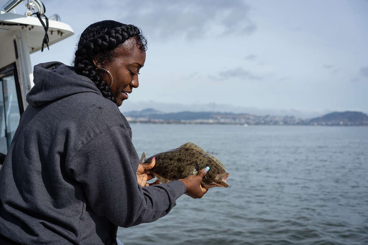 Myishia Haynes libera un halibut joven y jadeante de regreso a la bahía el jueves 26 de mayo de 2022. Las pescadoras frecuentemente capturaban halibut que no cumplían con el requisito de tamaño mínimo de 22 pulgadas y los devolvían a la bahía, a menudo animándolos a “ ¡Regresa y visítanos cuando seas un poco más grande, y asegúrate de contarles a tus amigos sobre nuestro sabroso cebo!” 