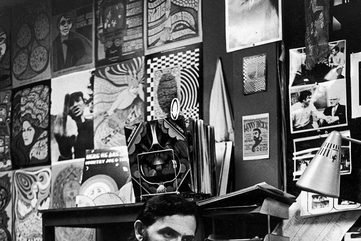  Bill Graham, productor y promotor de conciertos de rock, habla por teléfono en su oficina en el club de música Fillmore West, San Francisco, California, agosto de 1969. Las paredes están decoradas con carteles y fotografías de conciertos psicodélicos, y hay una pila de álbumes de discos. encima de una estantería. 