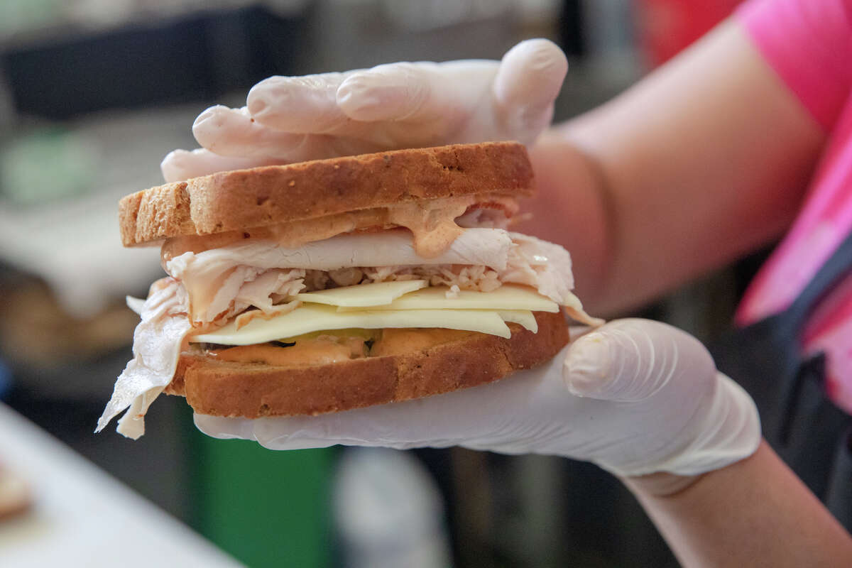 La empleada Bertha Due sostiene un sándwich de pavo con pepinillos y aderezo ruso que preparó en el mostrador de delicatessen de Ratto en Oakland, California, el 3 de agosto de 2022.