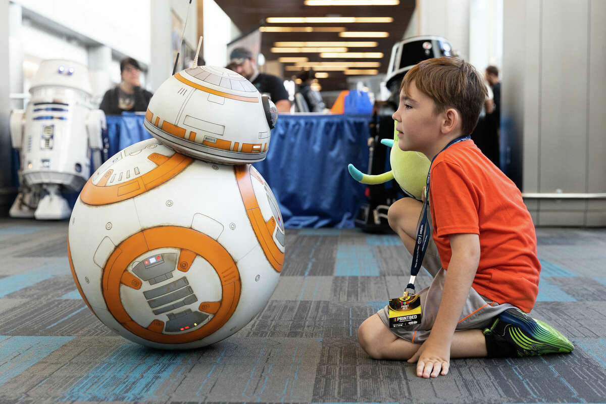 Tyler Swanson se arrodilla para mirar un robot BB-8 de "Star Wars" en SiliCon con Adam Savage en el Centro de convenciones San Jose McEnery el 27 de agosto de 2022. 