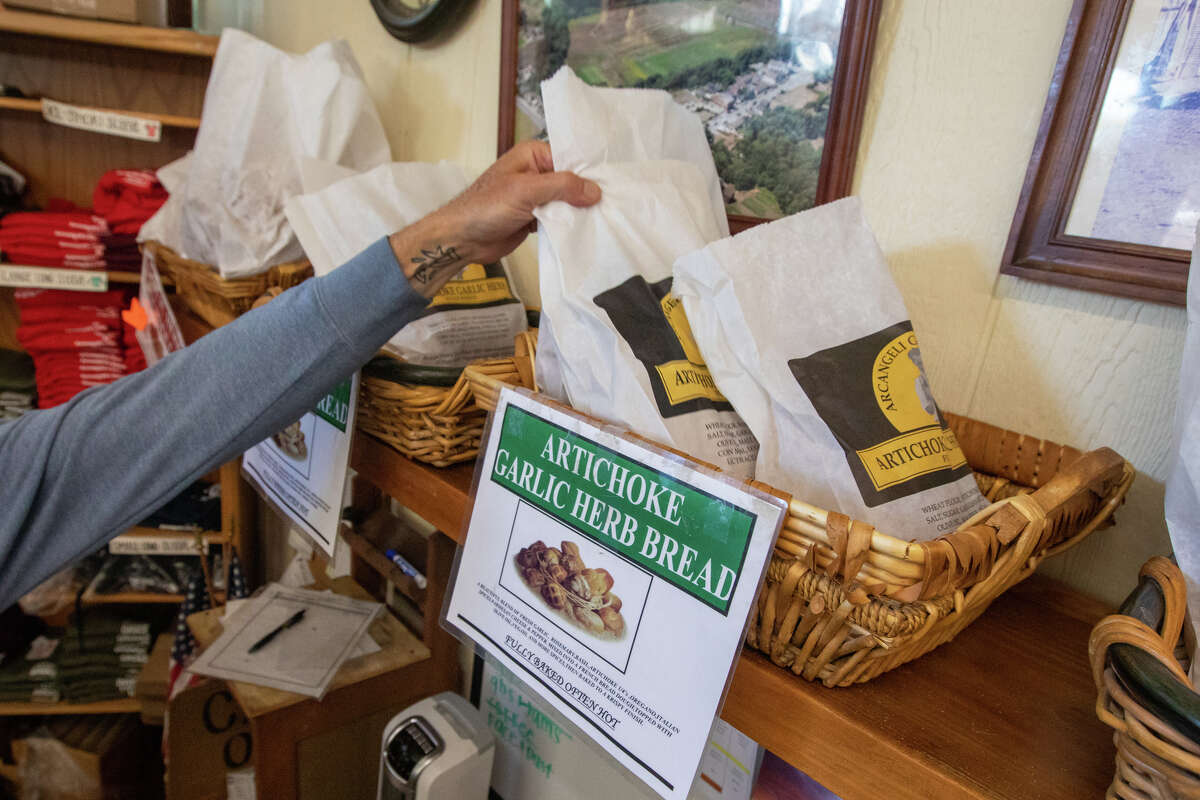 Un empleado de una tienda alcanza una bolsa de pan de alcachofas, ajo y hierbas recién horneado en Arcangeli's Grocery Co. en Pescadero, California, el 31 de agosto de 2022.
