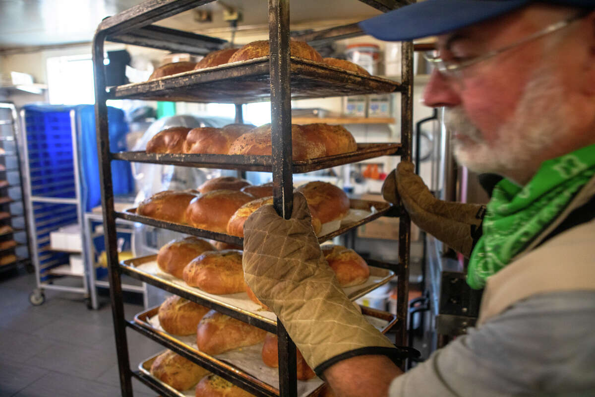 El panadero Tom Shuman saca pan de hierbas con ajo y alcachofa recién horneado en Arcangeli Grocery Co. en Pescadero, California, el 31 de agosto de 2022. La tienda hornea continuamente el pan fresco todo el día para los clientes.