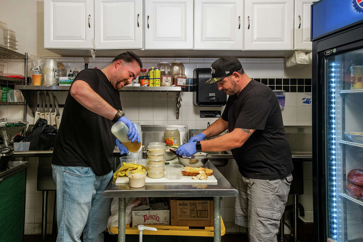 Mohannad Alkhouri, a la izquierda, y Joey Jada producen tamaños para llevar de su firma Hella Hummus que se ofrece en una variedad de sabores en McBaker Market & Deli en San Francisco el viernes 12 de agosto de 2022 por la tarde.