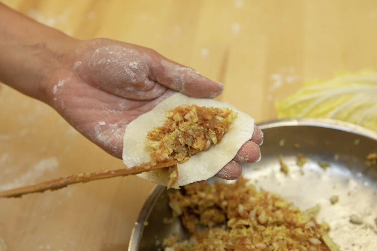 Sandy Zheng coloca el relleno de repollo napa y cerdo en el envoltorio de bola de masa hervida para las pegatinas de olla de cerdo de la abuela para las bolas de masa hervida unidas en San Francisco, California, el 29 de agosto de 2022.