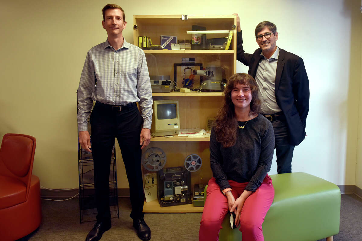 Desde la izquierda, Daniel Johnson, Robyn Ollodort y Andrew Roderick aparecen en el Departamento de Tecnología Académica de SFSU junto a una vitrina de varias reliquias tecnológicas.