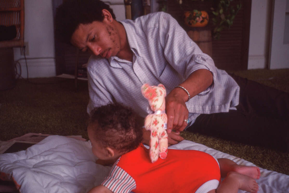 “Raymond Cooper jugando con su hijita, Aja Cooper”. a “Raymond Cooper jugando con su hijo pequeño, Ahmed Cooper”.