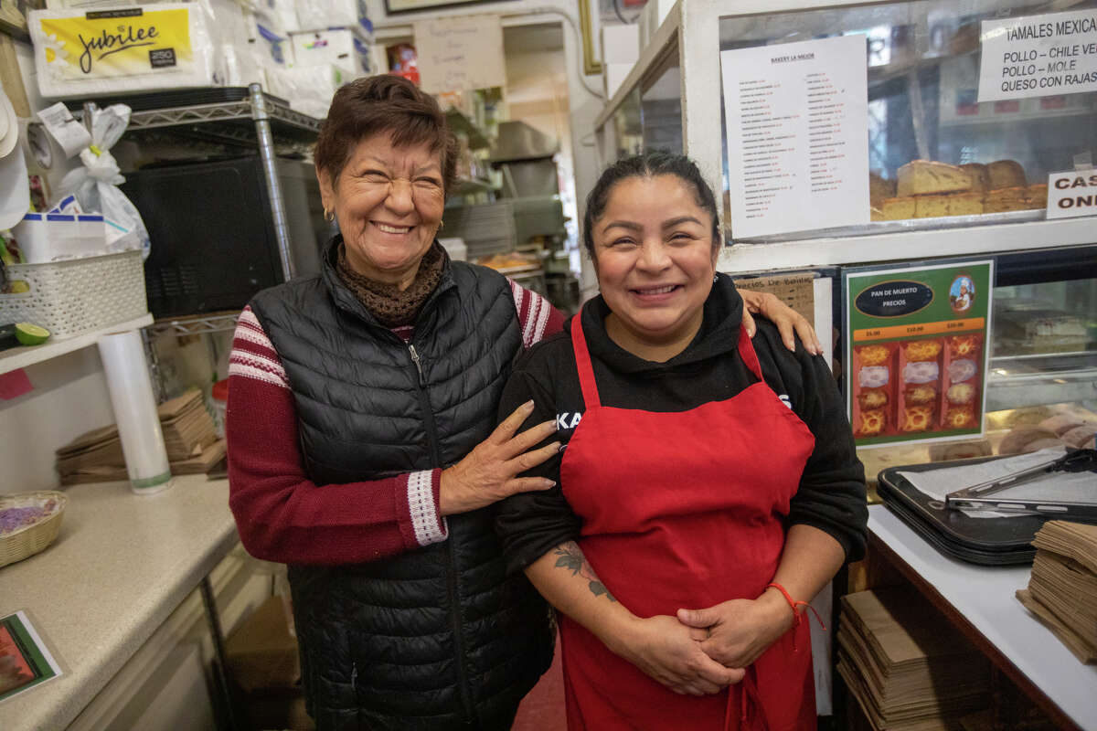 La propietaria Carmen Elias comparte una risa con la empleada Lisenia Rivera detrás del mostrador en La Mejor Bakery en el Distrito de la Misión de San Francisco el 27 de octubre de 2022.