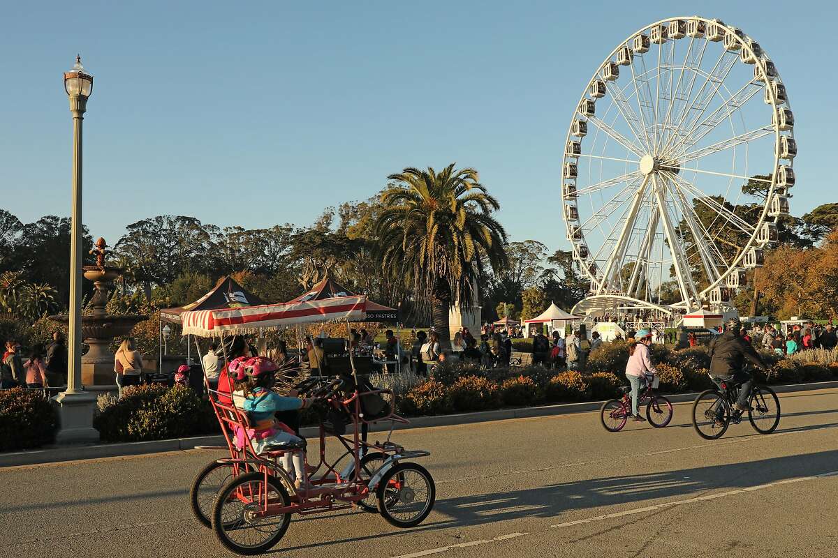 Los ciclistas pasan junto a una larga fila de personas para la rueda de observación SkyStar Golden en el Golden Gate Park el 28 de noviembre de 2020 en San Francisco, California.