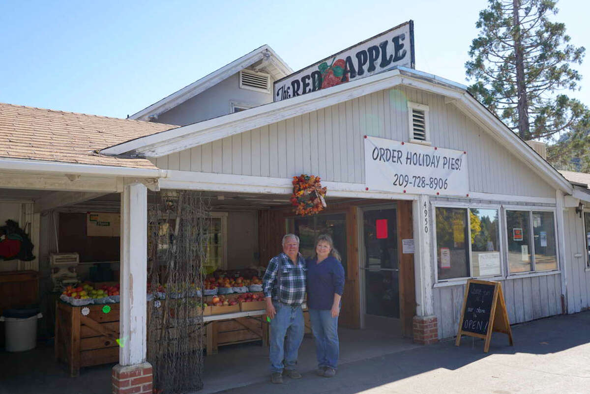 Los propietarios de Red Apple, Christy y Lloyd Bunch, posan frente a su negocio de décadas de antigüedad, Red Apple. El puesto de frutas y panadería al borde de la carretera, en 4950 CA-4 en Murphys, California, se especializa en pasteles de manzana caseros y donas de sidra de manzana. 
