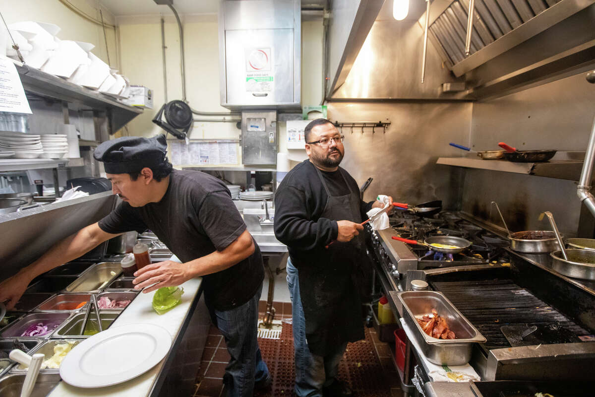 Nelson Ortiz, a la izquierda, y German Deras preparan comidas en la cocina de Rudy's Can't Fail Cafe en Emeryville, California, el 4 de noviembre de 2022.