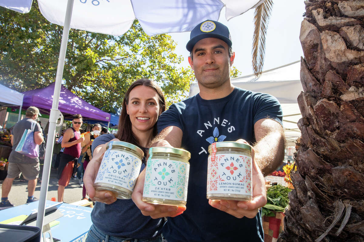 Los propietarios Katia Berberi y su esposo Steve Drapeau sostienen parte de su salsa toum en el puesto de Anne's Toum en el mercado de granjeros de Grand Lake en Oakland, California, el 20 de agosto de 2022. Su toum, una salsa de ajo libanesa, se basa en la receta de la familia materna de Katia. .