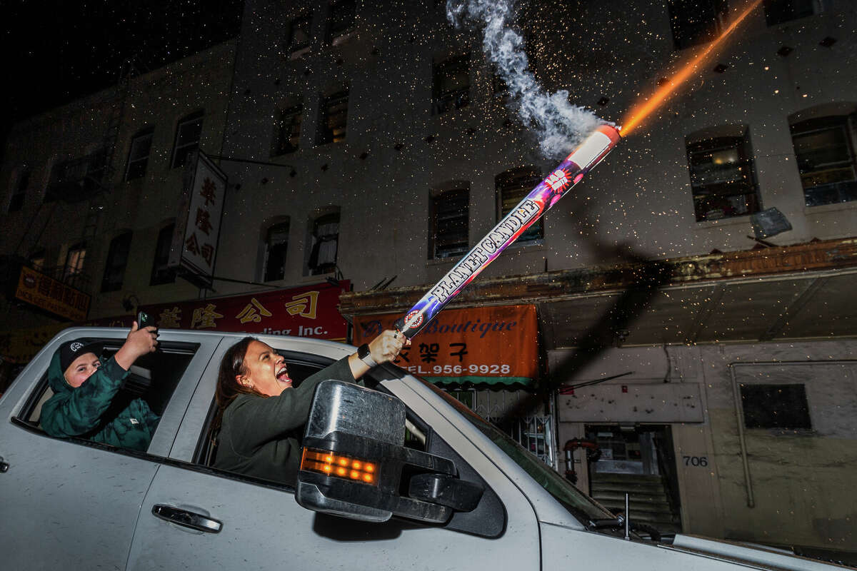 Una mujer lanza fuegos artificiales hacia el cielo de la tarde desde un camión en Jackson Street en medio de las festividades de la víspera del Año Nuevo Lunar en Chinatown el sábado 21 de enero de 2023 por la noche.