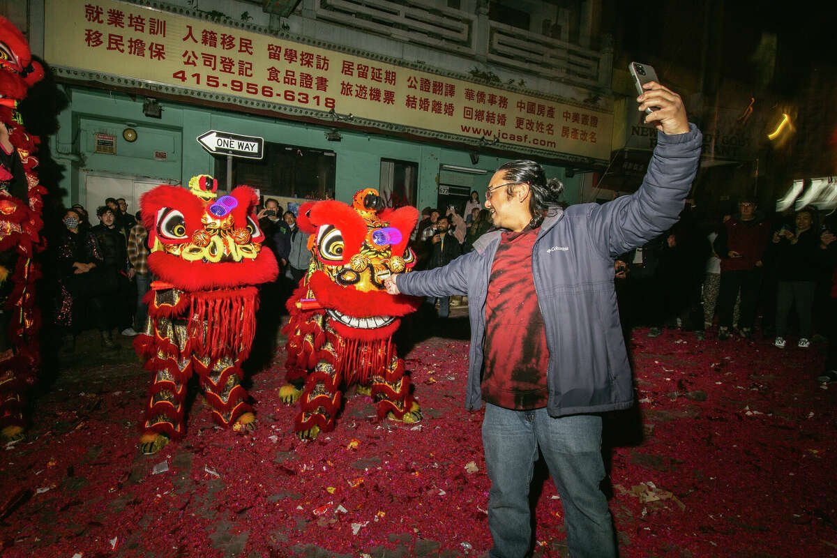 Un hombre se toma una selfie con los tradicionales bailarines del león de San Francisco en Jackson Street en medio de las celebraciones del Año Nuevo Lunar en Chinatown el sábado 21 de enero de 2023 por la noche.