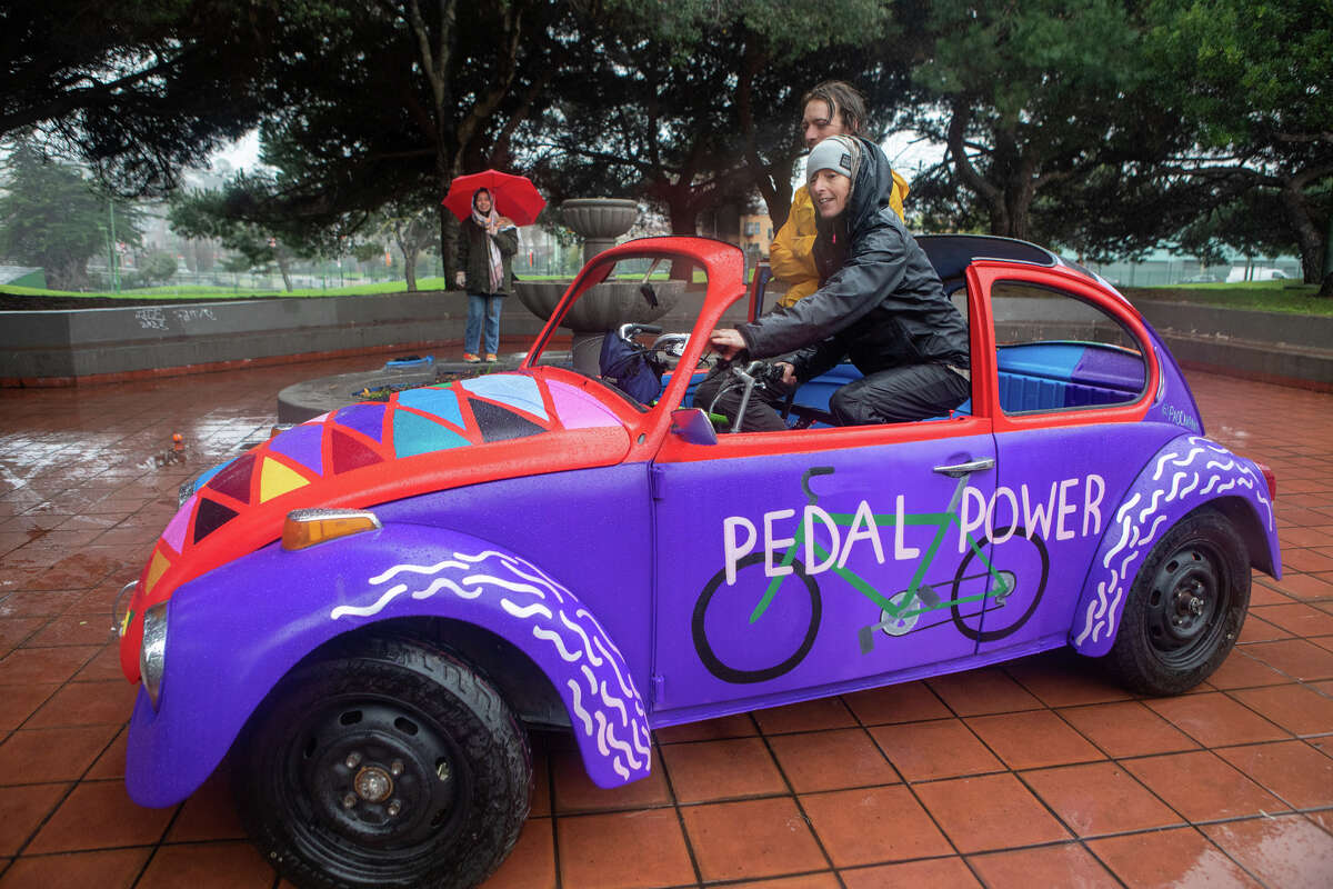 Deborah Gutof (al frente) conduce un auto-bicicleta creado por Eric Schmidt (izquierda) fuera del armazón de un VW Beetle de 1971 llamado "Pedal Power" en el Parque Potrero del Sol en San Francisco el 11 de enero de 2023. El vehículo funciona con energía humana de dos bicicletas montadas dentro del vehículo.