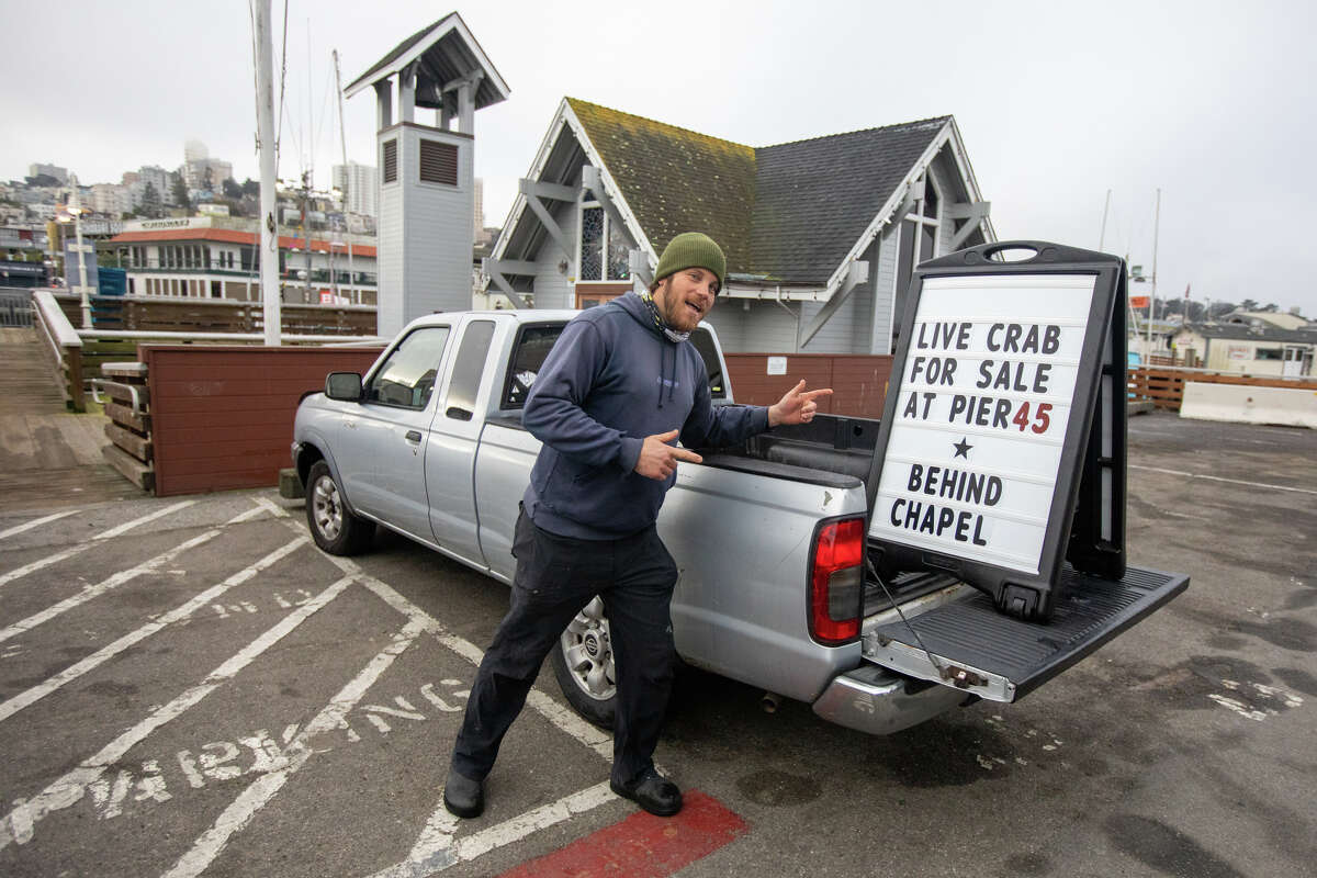 Un miembro de la tripulación del barco de pesca de cangrejos Willanina señala un letrero que indica al público dónde comprar cangrejos Dungeness recién capturados en el Muelle 45 en Fisherman's Wharf en San Francisco el 27 de enero de 2023.