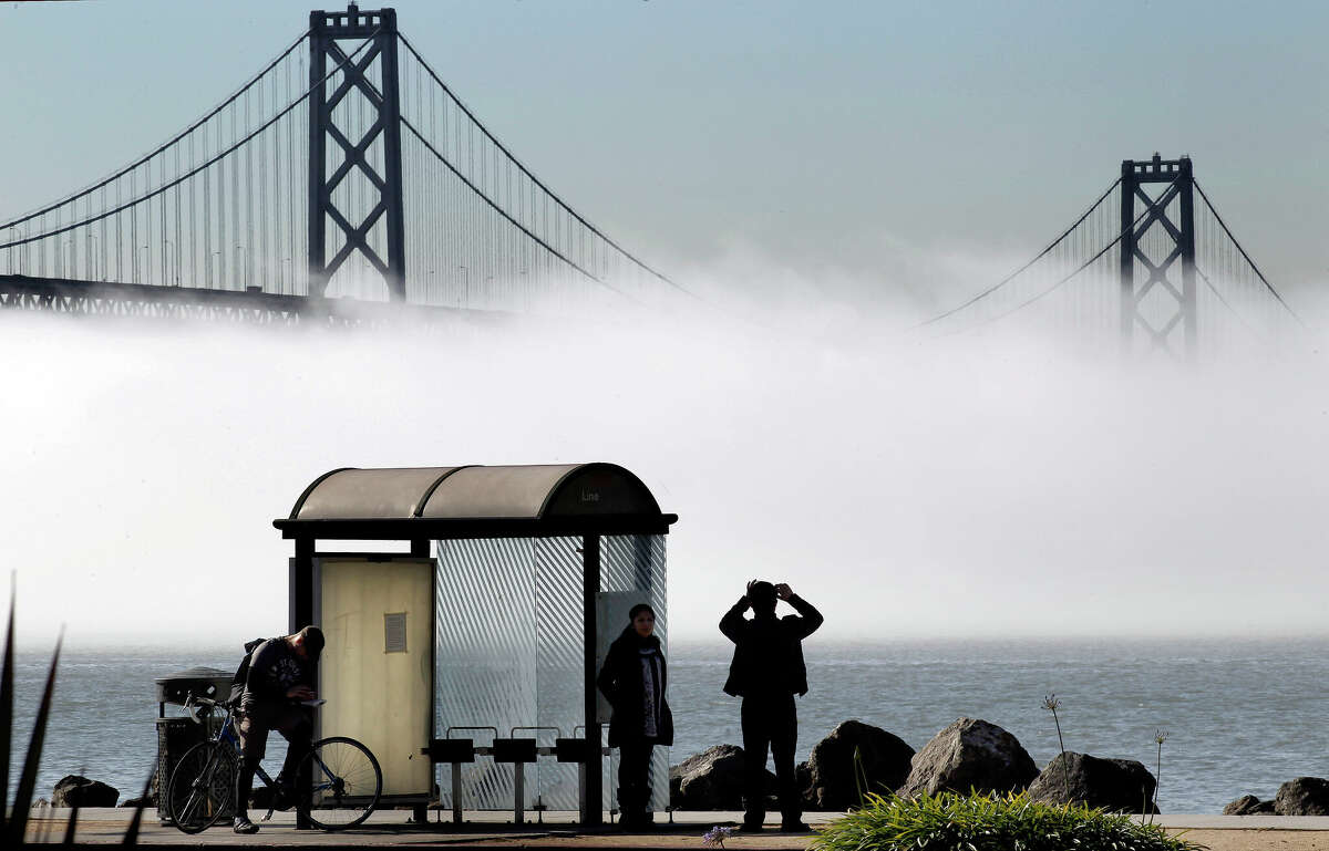 Los transeúntes se detienen para admirar la espesa niebla que pasa por debajo del Puente de la Bahía, como se ve desde una parada de autobús de Treasure Island en San Francisco, California, el viernes 27 de enero de 2012.