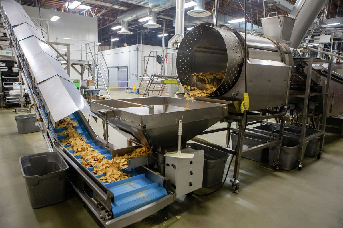 Chips de tortilla recién fritos caen de una freidora a una cinta transportadora en la planta de fabricación de Casa Sánchez en Hayward, California, el 15 de febrero de 2023.