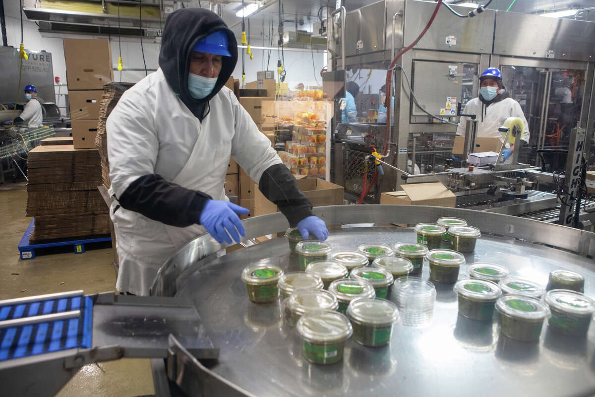 Un trabajador ayuda a colocar cubiertas en los paquetes de salsa recién hecha en la planta de fabricación de Casa Sánchez en Hayward, California, el 15 de febrero de 2023.