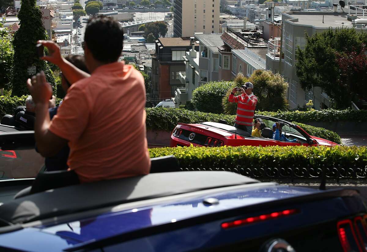 Los turistas toman fotografías mientras conducen por Lombard Street en San Francisco, California.