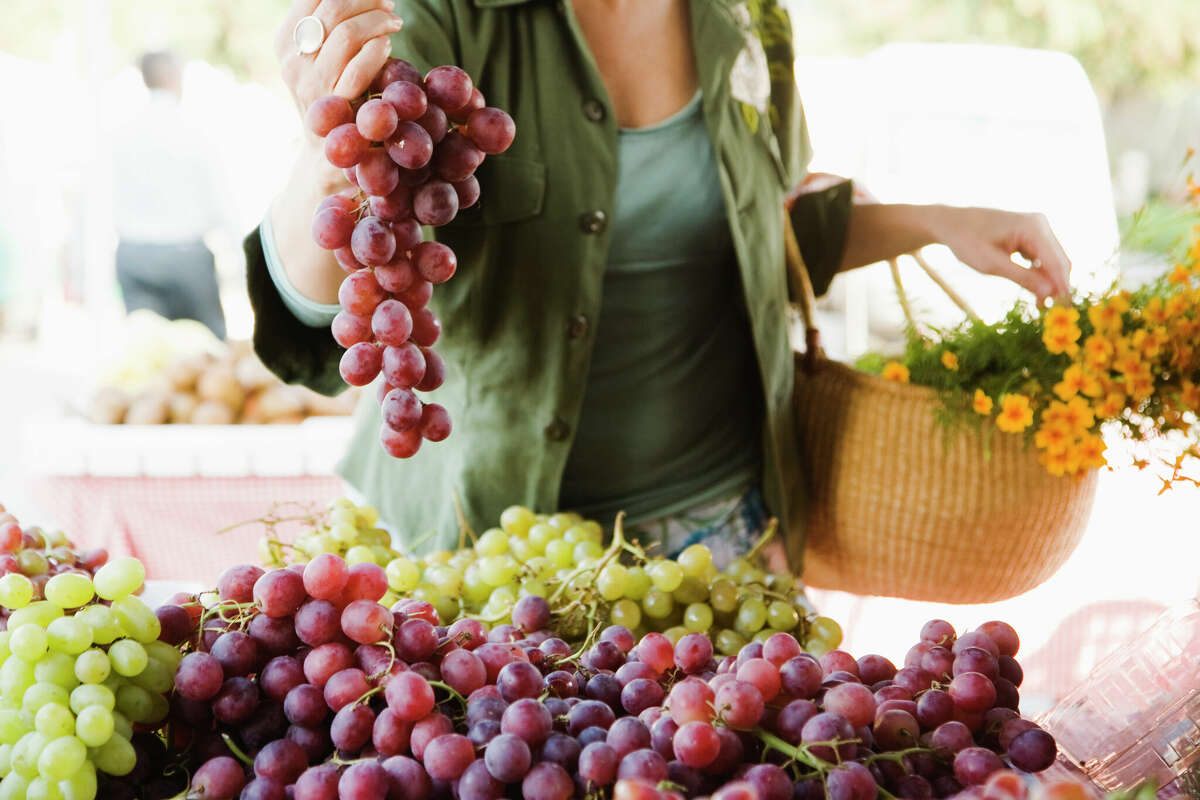 Una mujer recoge uvas en un puesto del mercado de agricultores.