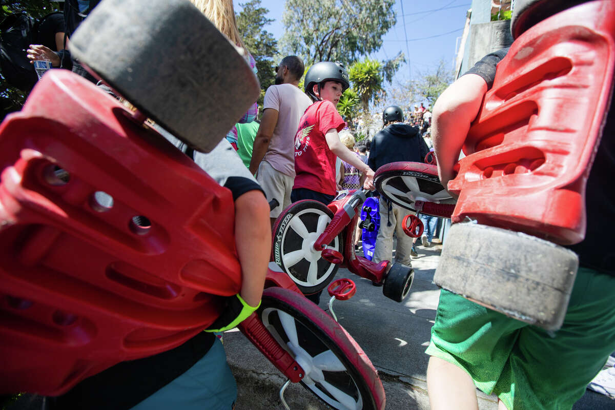 Los niños cargan las ruedas grandes de regreso por las escaleras para montar otra serie del evento de carrera Bring Your Own Big Wheel en Vermont Street en San Francisco, California, el 9 de abril de 2023.