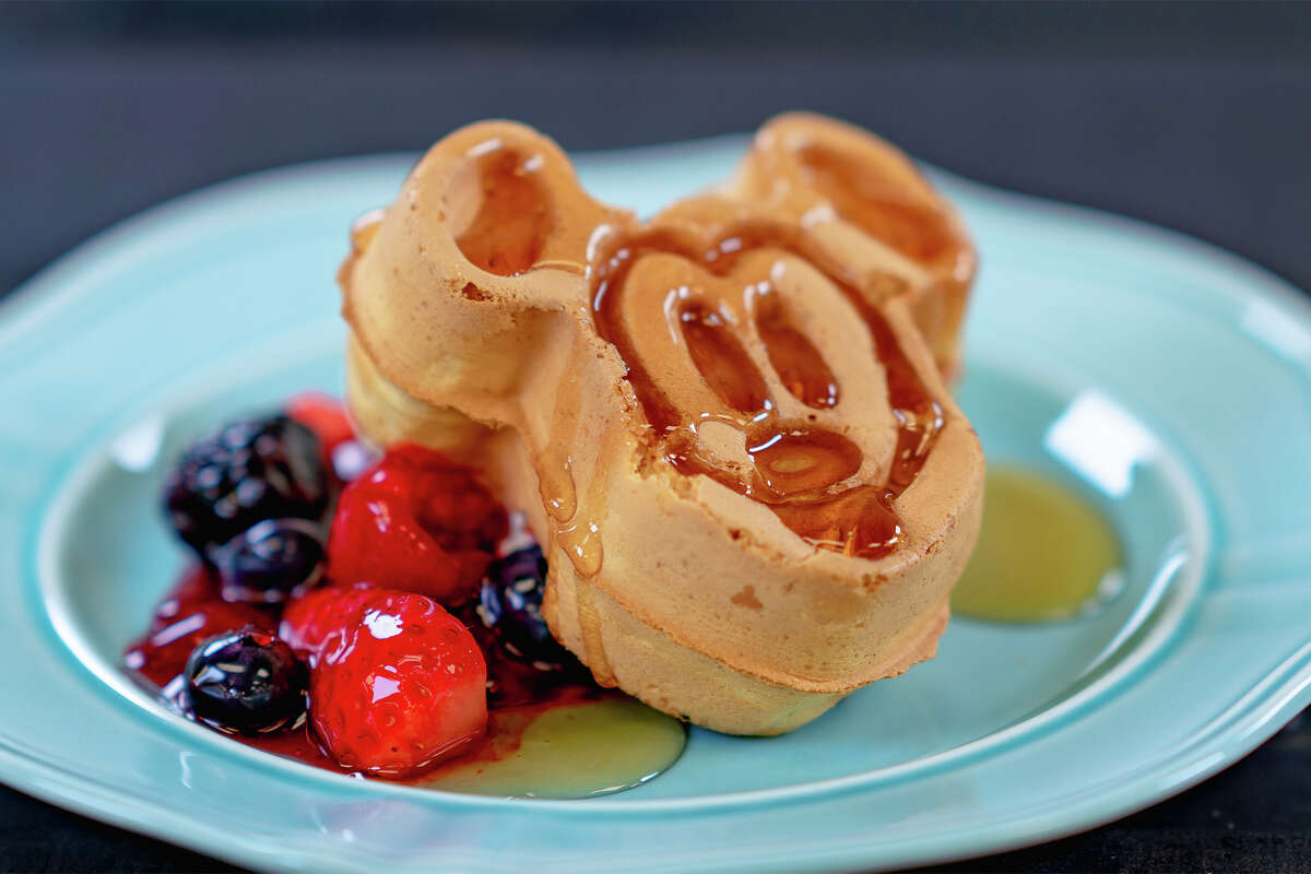 Los famosos Mickey Waffles de Disneyland se muestran en un plato azul con bayas frescas y almíbar.