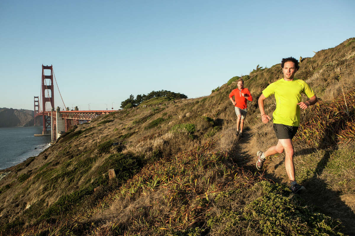 Dos hombres corren cerca de Baker Beach con vistas al puente Golden Gate.