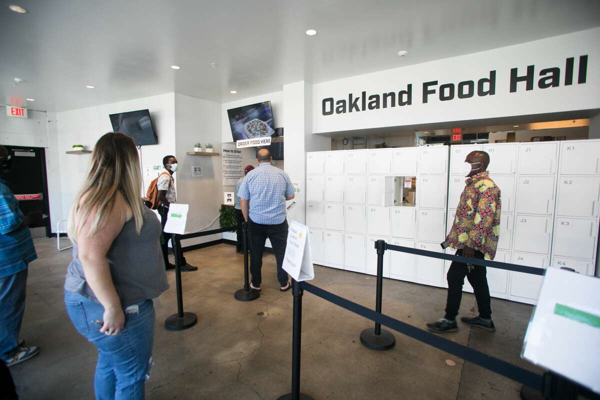 Los clientes esperan para recoger los pedidos de comida de Oakland Food Hall en East 12th Street en Oakland el 30 de julio de 2021. La instalación de "cocina fantasma" alberga diferentes cocinas comerciales que hacen pedidos para llevar para los clientes.