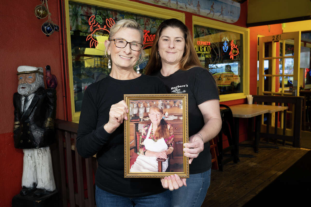 Melodie Madsen y Amanda Howard sostienen una foto de Barbara Walsh, tres generaciones de propietarios de Barbaraʻs Fishtrap en Half Moon Bay California, 4 de mayo de 2023