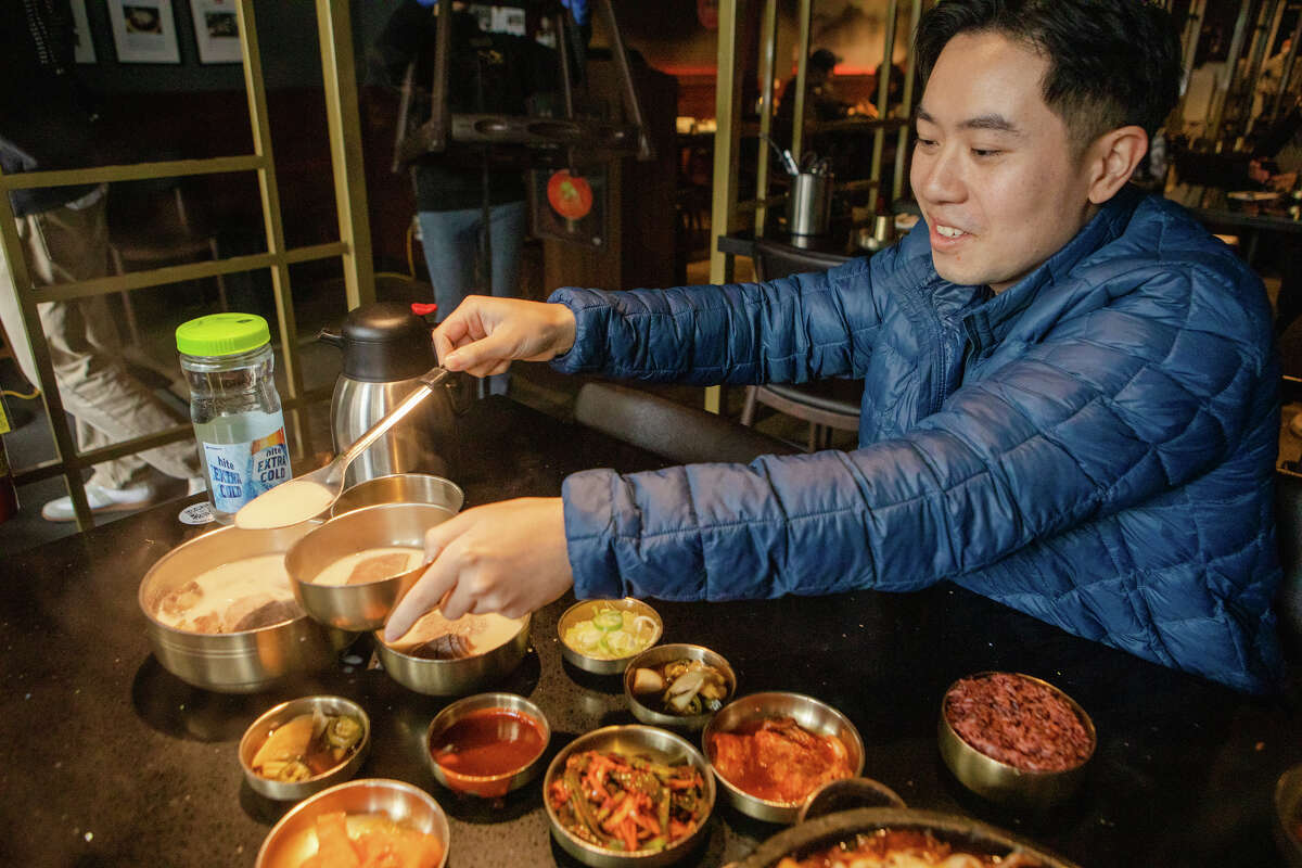 Tim Cheung de Bay Area Foodies vierte un poco de caldo de Suyuk, rebanadas de carne hervida en una sopa de hueso de buey de color blanco lechoso en Daeho Korean BBQ & Beef Soup el 9 de mayo de 2023. Es una persona influyente en las redes sociales con cientos de miles de seguidores en Instagram y Tik Tok.